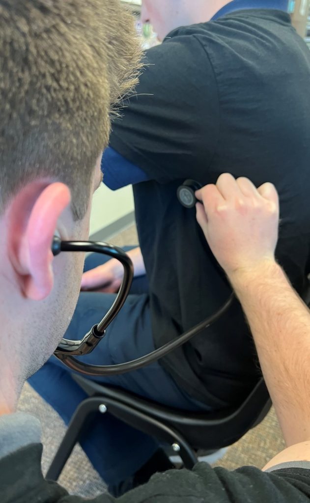 A person using a stethoscope to listen to a patient's left mid-axillary line, left mid-lung.