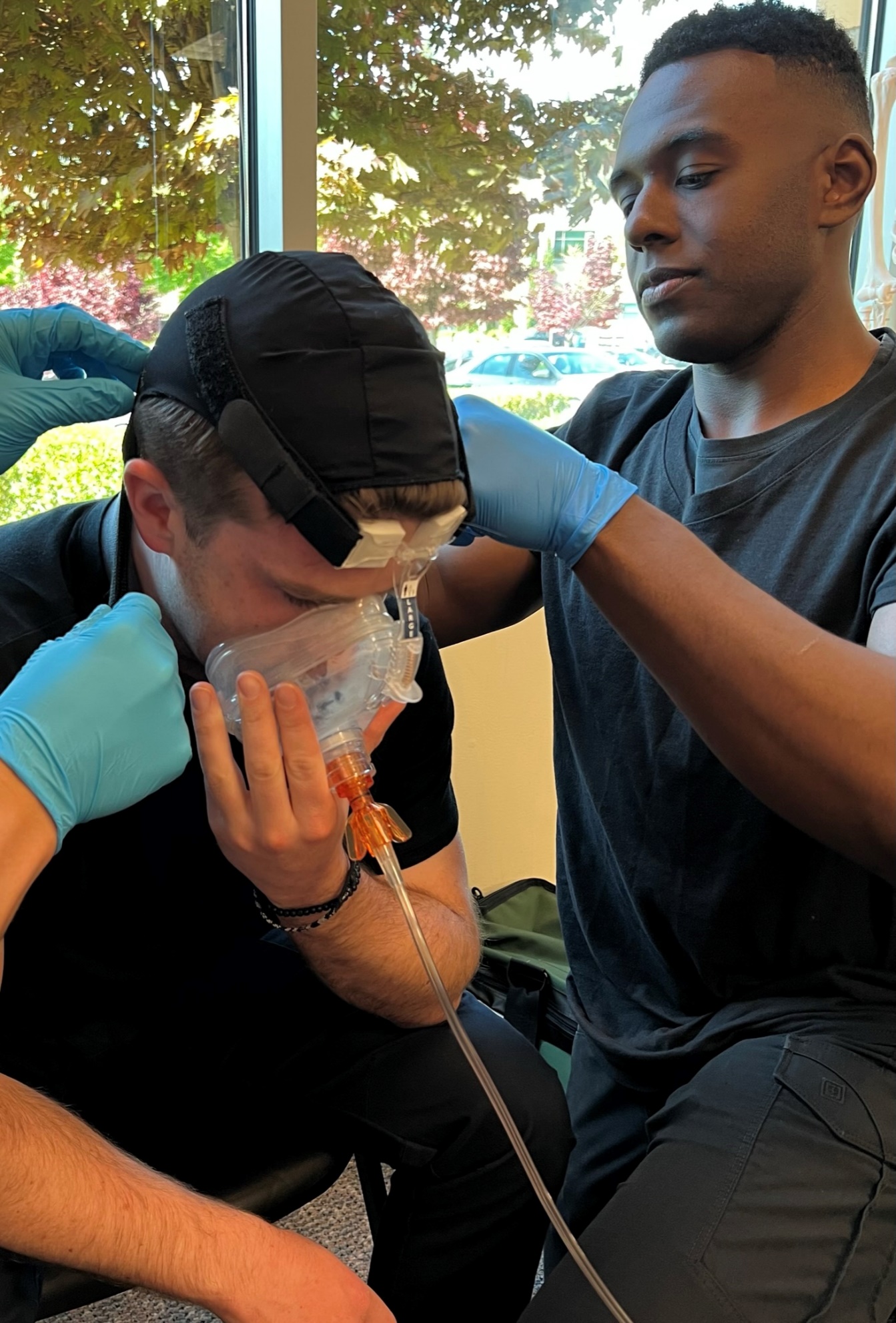 Two gloved EMTs placing a CPAP mask to a seated patient.