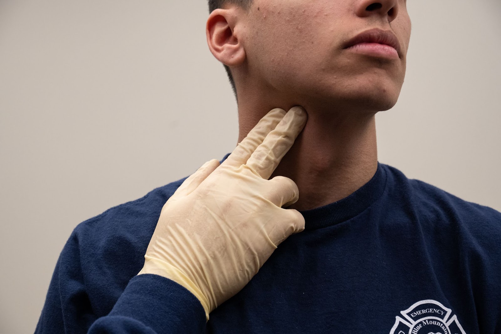 imageA man wearing a glove places his right hand with pointer and middle fingers pressing into the right side of his neck, to the right of his Adam's apple.to locate carotid artery