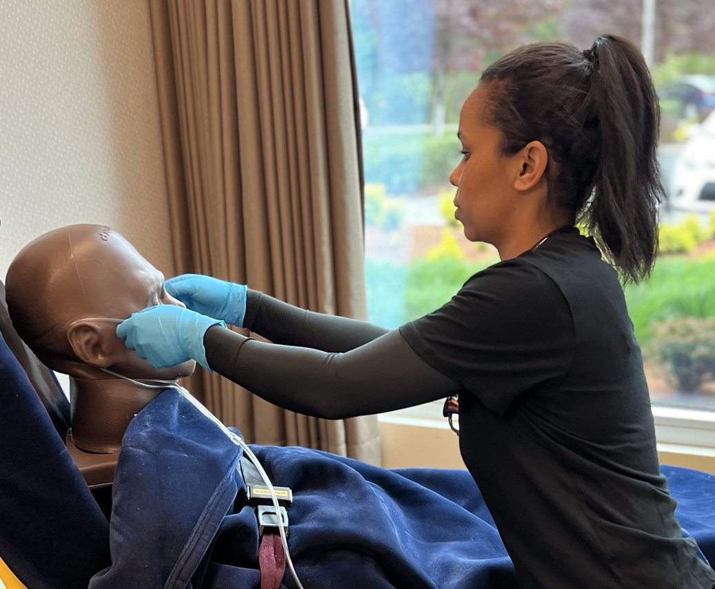 A photo of a gloved EMS clinician placing the prongs of the nasal cannula into the nose on a simulated patient.