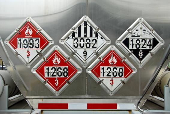 A truck bearing the hazardous materials placards: code 1993 with the red number 3 below it, 3082 with black 9 below, 1824 with white 8 below, 1268 with white 3 below, 1268 with a red 3 below.