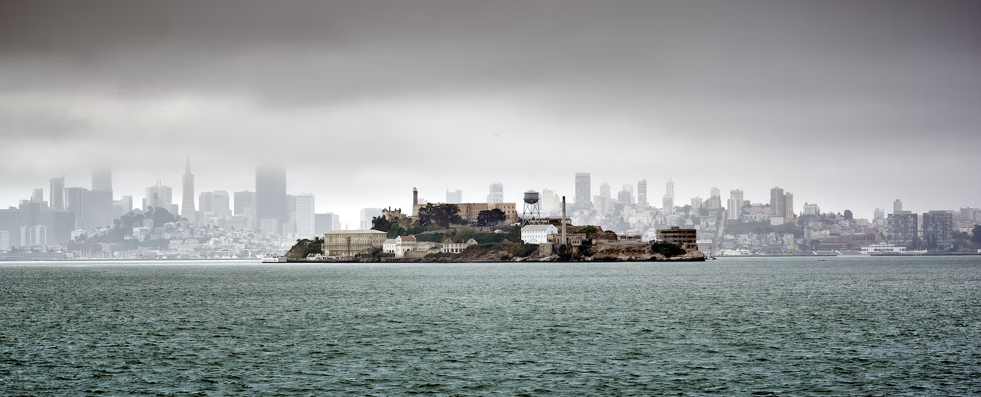 A photograph of the iconic Alcatraz prison, known as the “rock” in front of the San Francisco skyline.