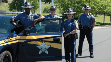 Photograph of four Oregon State Troopers posing with a Patrol car.