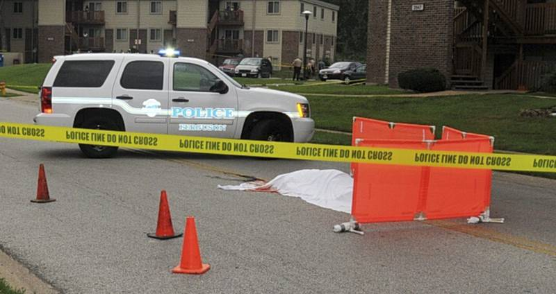 An evidence photograph from Ferguson Police Department’s Michael Brown Crime Scene showing crime scene tape surrounding a patrol car, cones, a temporary orange barrier and a white sheet with blood stains at one end covering the deceased body of Michael Brown.