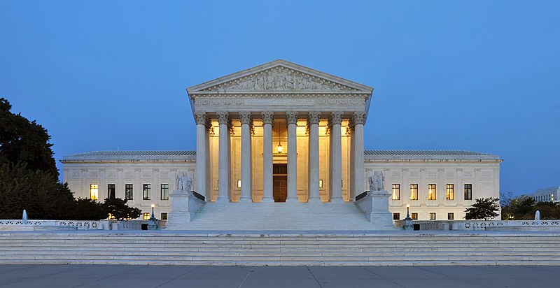 The US Supreme Court is a white marble structure with pillars illuminated at dusk.