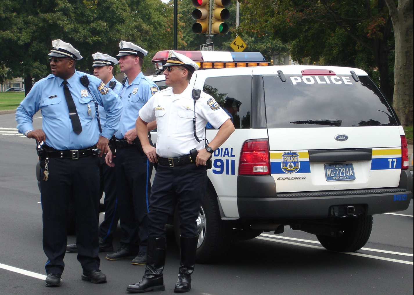A photo of four Philadelphia police officers in uniform standing in the roadway next to a marked patrol explorer.