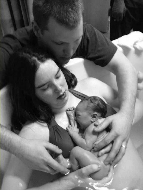 Father’s arms around mother and newborn in tub
