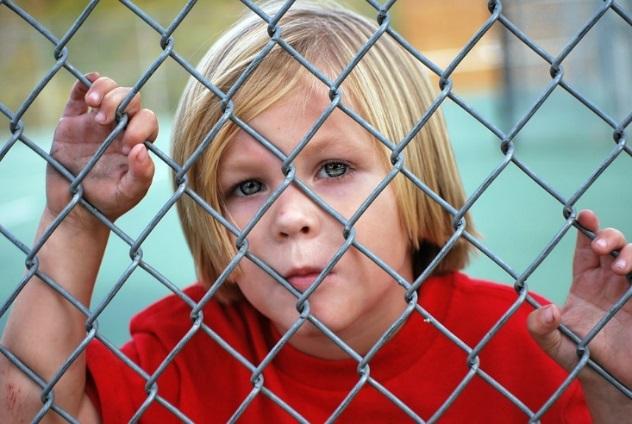 Boy standing with hands and face pressed up against chain link fence