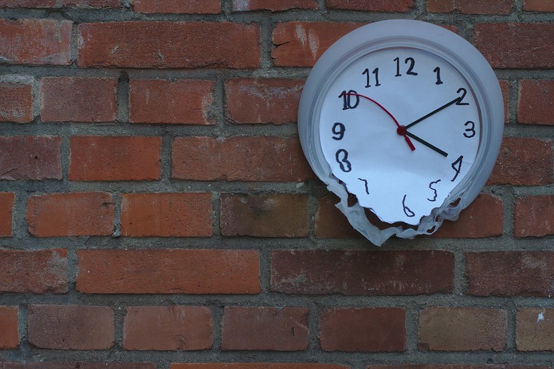 The plastic face of a clock melts against a brick wall