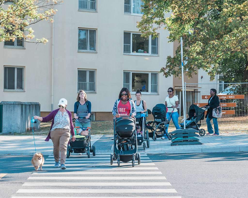 A group of parents push strollers from a sidewalk into a crosswalk.