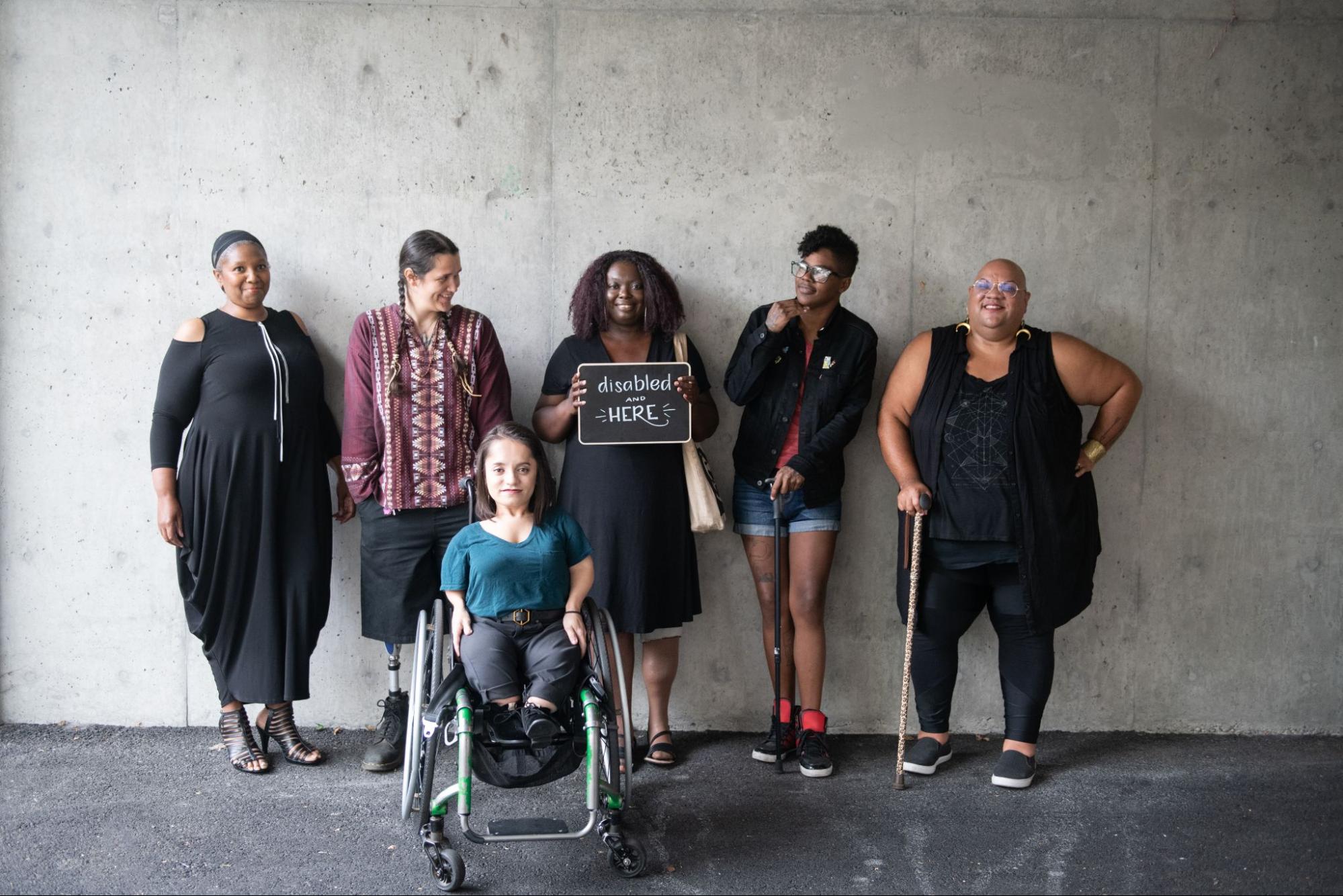 A group of people of color with a range of disabilities pose together. Image Description Available.