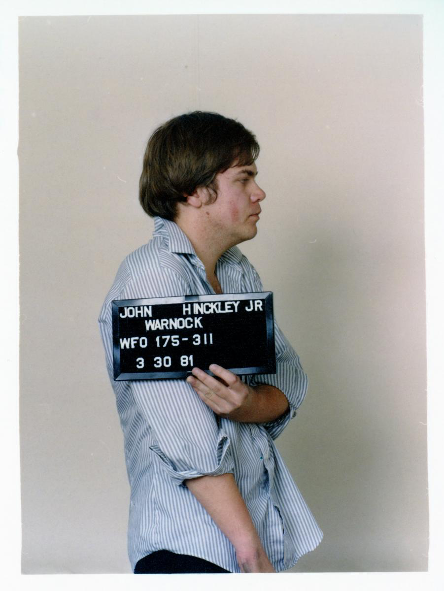 John Hinckley, Jr. holding identifying sign in his 1981 mugshot,