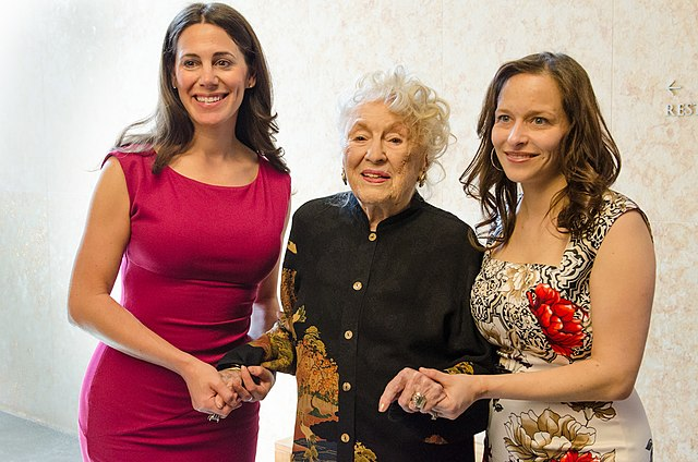 Three women hold hands, the woman in the middle being elderly and the two at her sides middle aged