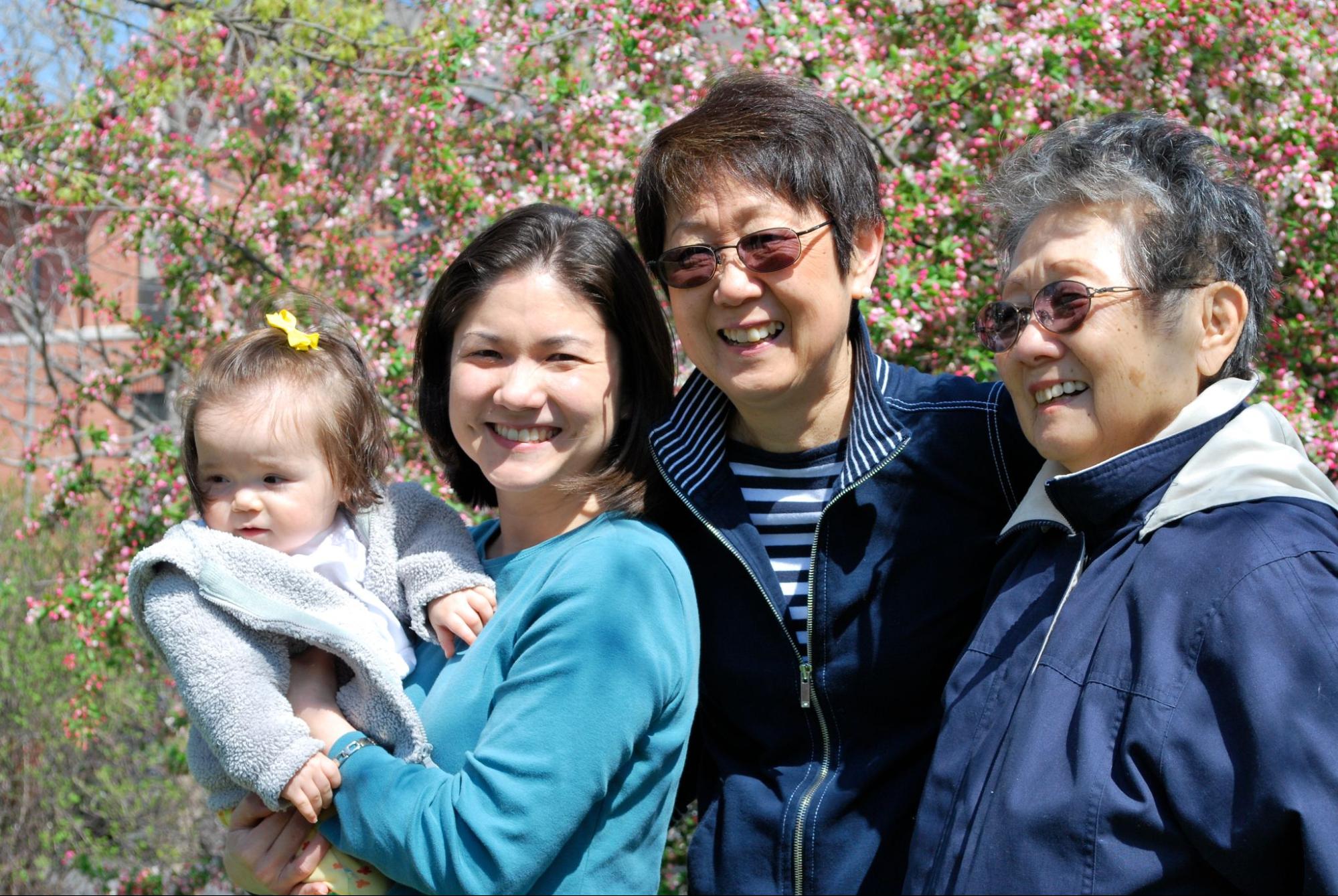 A group of women including a young girl, her mother, her grandmother and her great grandmother stand in front of blooming plants.