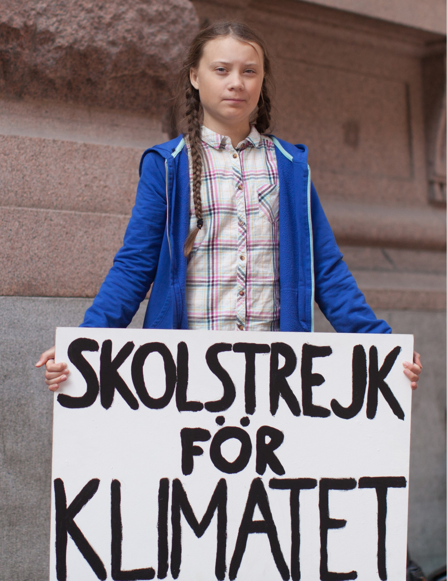 Greta Thunberg holding a sign that says "school climate strike" in Swedish