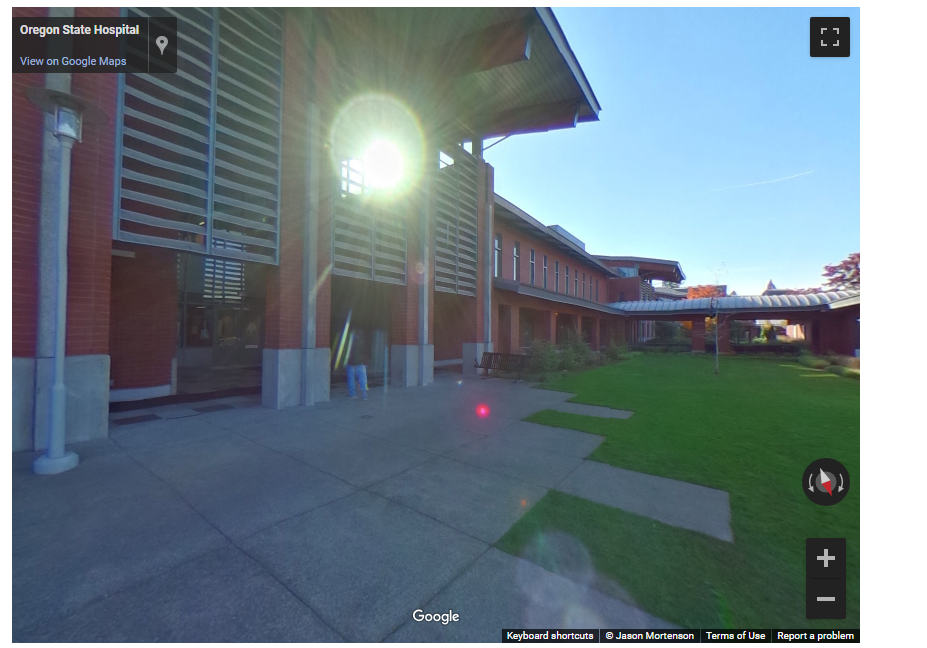 The modern two story brick building has a concrete patio and a grassy area surrounding it. You can also see a covered walkway and a roof that protects the patio.