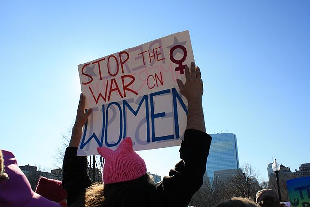 People wearing pink knit hats carry signs that say Stop the War on Women