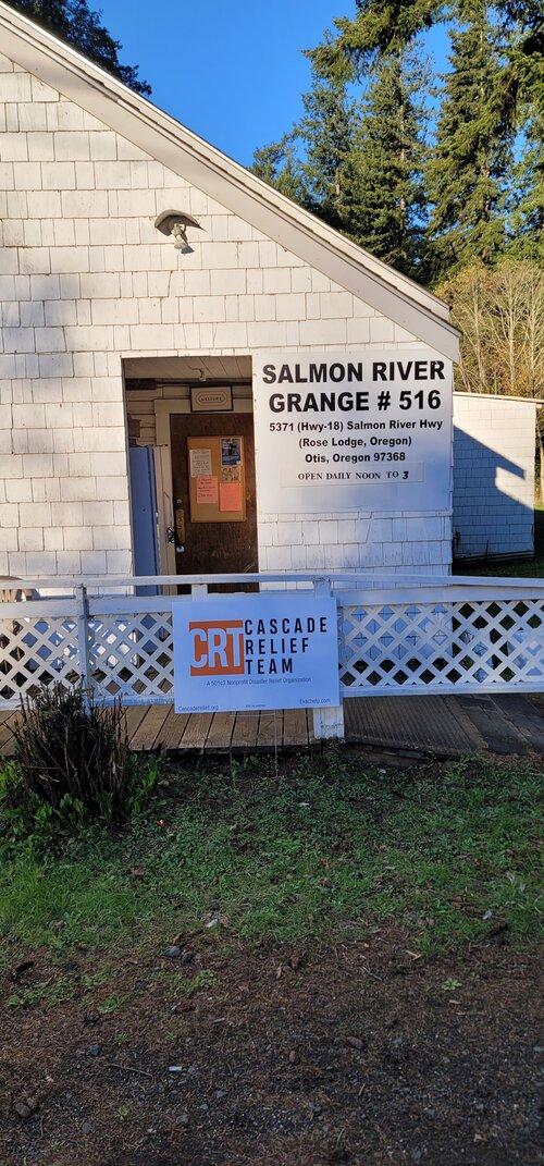 A white clapboard building with a sign on the front that says "Salmon River Grange #516". In front of the building there is also a sign that says "Cascade Relief Team"