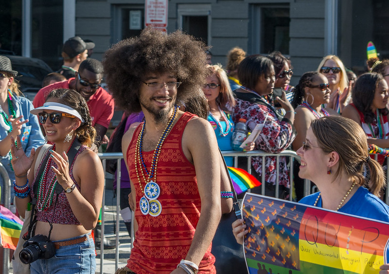 People wearing bright clothes and beads smiles as they carry rainbow flags down the street