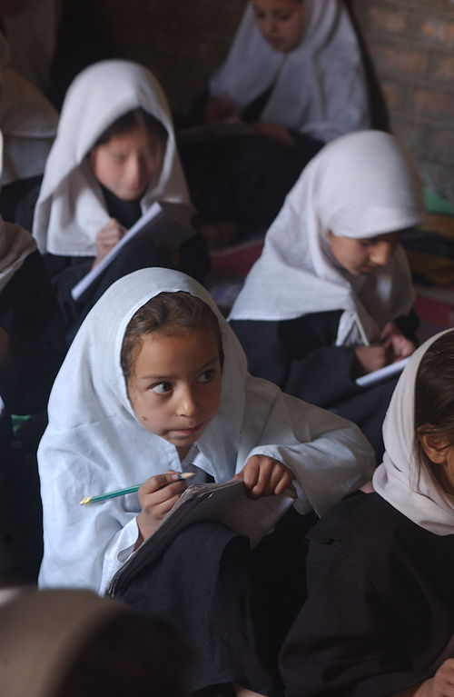 Young girls wearing chadors face in a single direction taking notes on paper