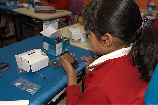 A young girl in a red sweater and ponytail holds a new digital device in her hand