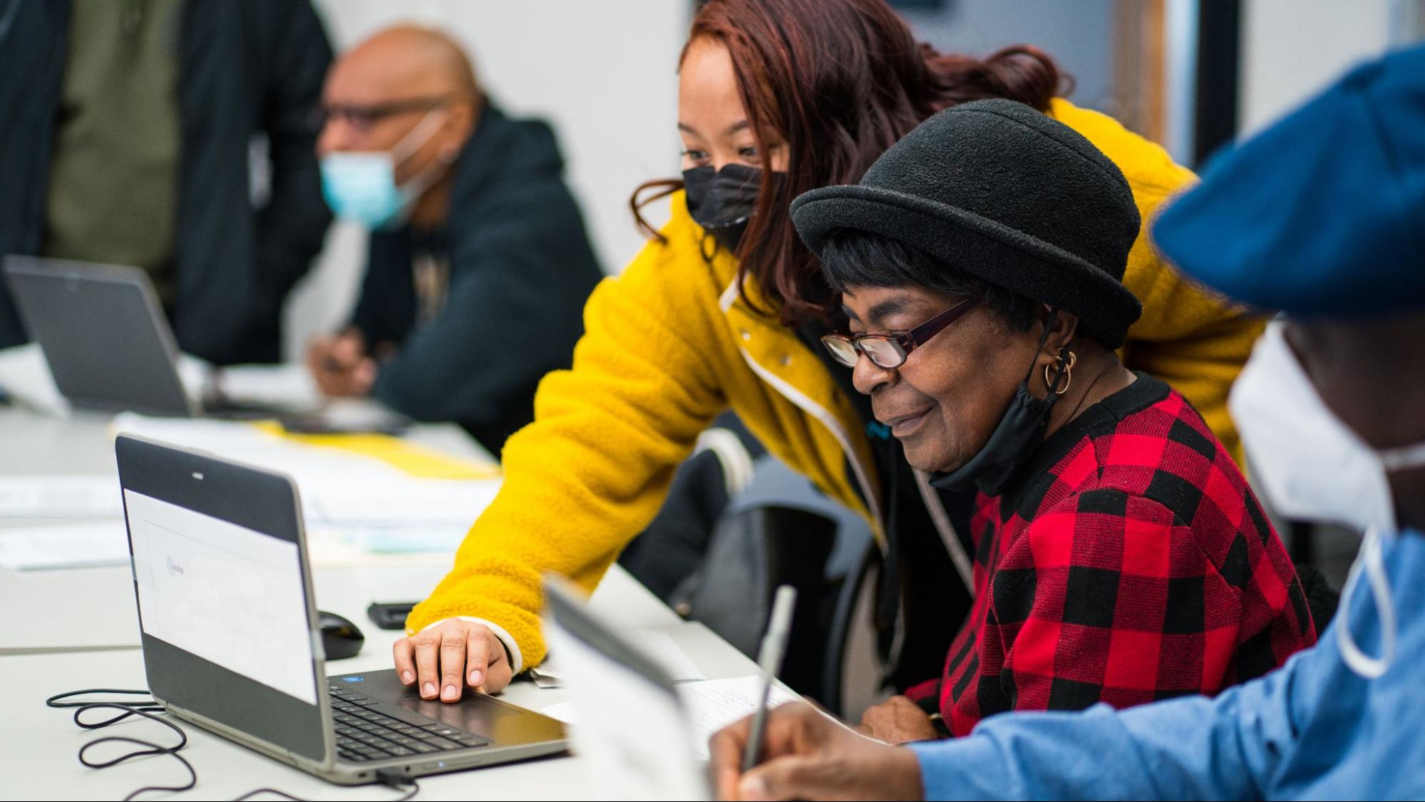 a teacher helps a student to use a computer. Both the teacher and the student have dark skin.