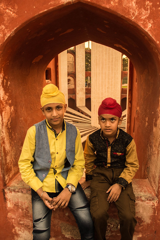 Two young boys wearing turbans that match their modern clothing sitting in a windowsill