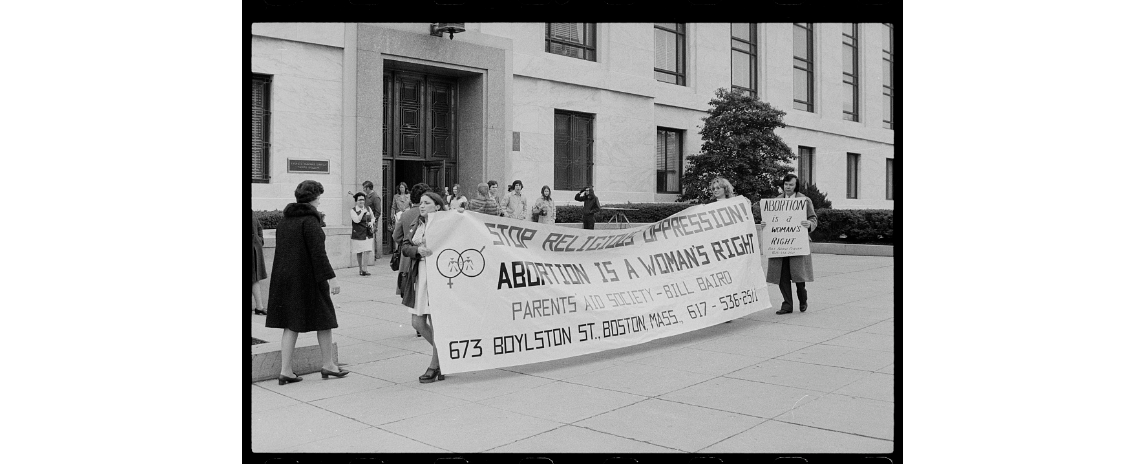 An archival black and white image of people marching with signs advocation for abortion as a woman's right