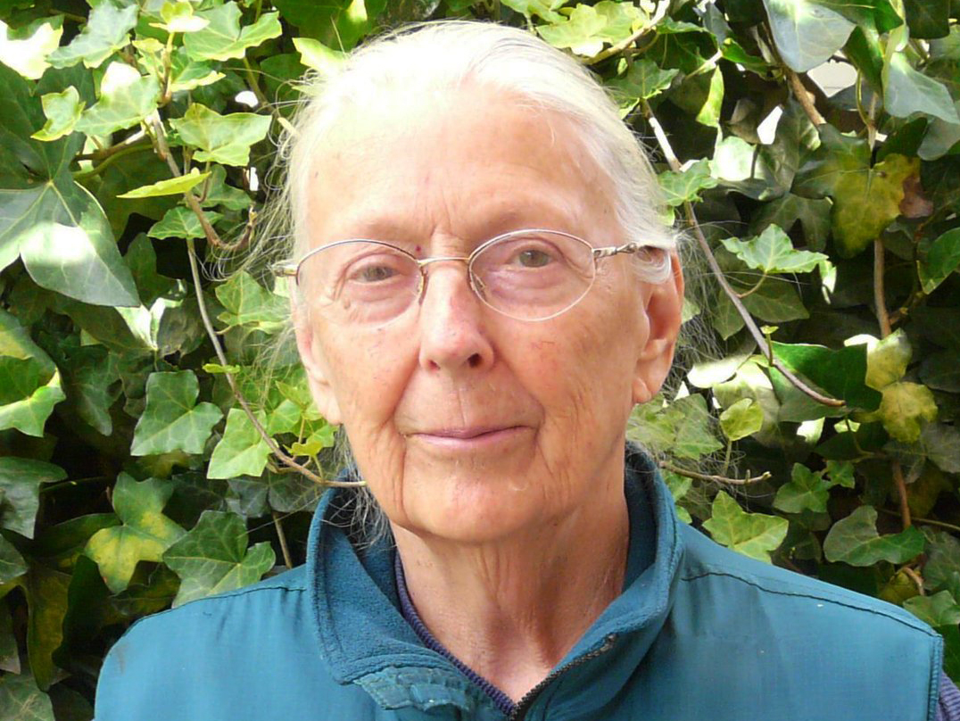 Dr. Dorothy Smith stands in front of a wall of ivy, has white hair, and wears glasses.