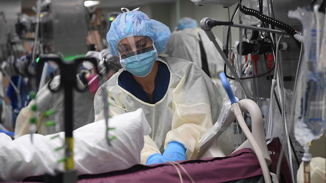 Fig 7.3 Medical provider wears protective gear. Their mouth and nose is covered by a mask, and their face is covered by a shield. They are helping a patient on a bed in front of them.