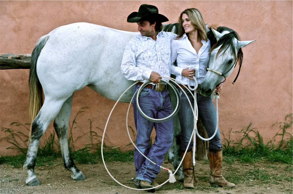 Two people wearing jeans and cowboy boots, holding a haltered horse by the lead rope.