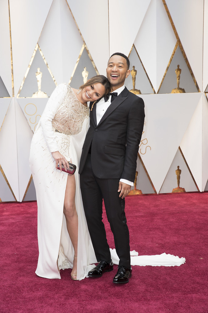 John Legend and Chrissy Tiegen embracing at a red carpet ceremony.