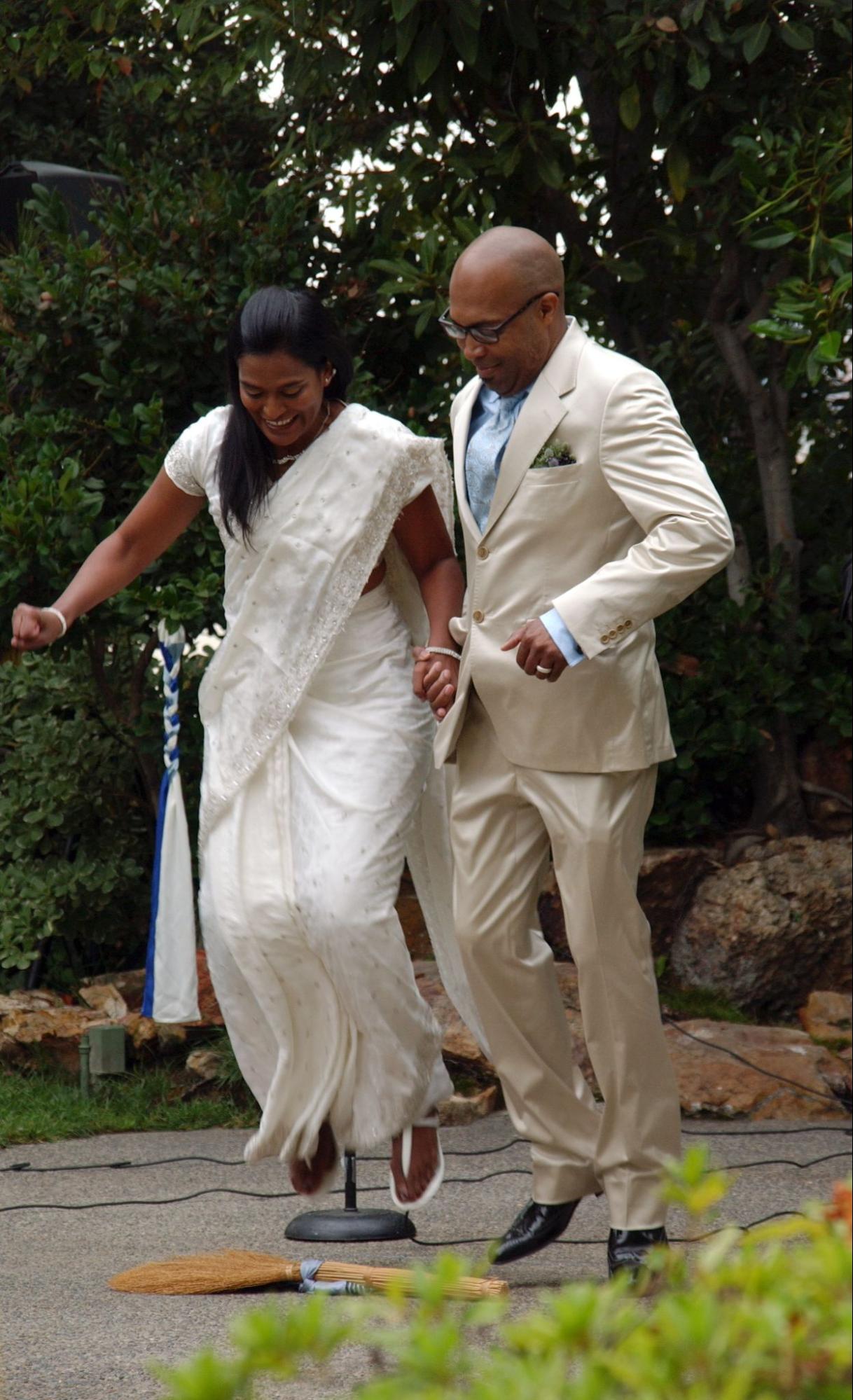 An African-American couple jumping over a broom at their wedding.