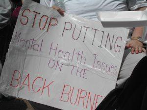 Poster with hand written message "Stop putting mental health issues on the back burner"