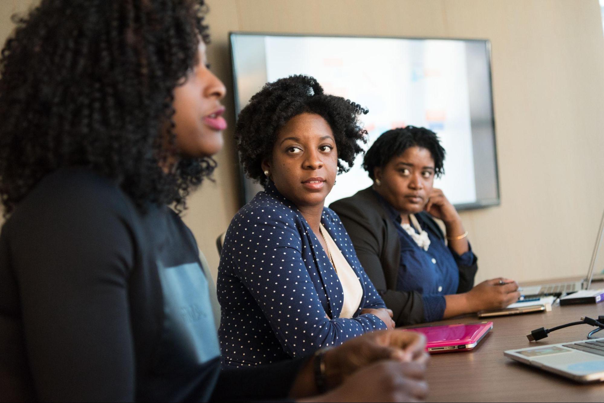 Black women with non-Eurocentric hairstyles talking at a business meeting.