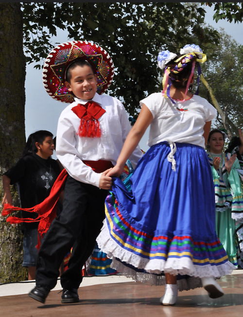 Two children dancing in traditional Mexican clothes.