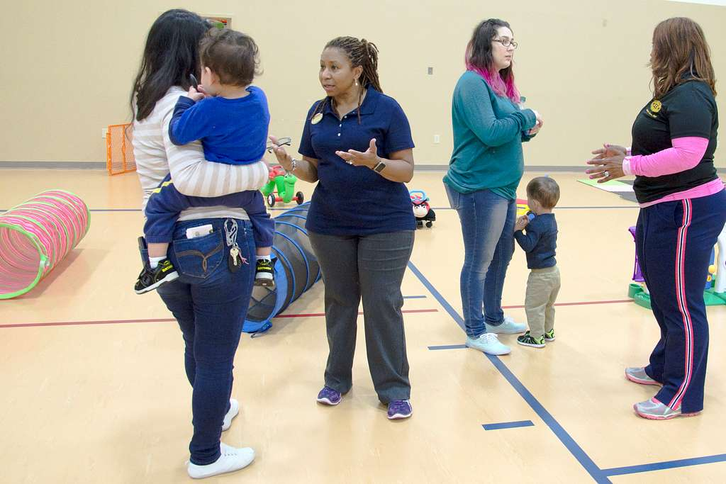 Parents and children playing in a gym and talking with staff members.