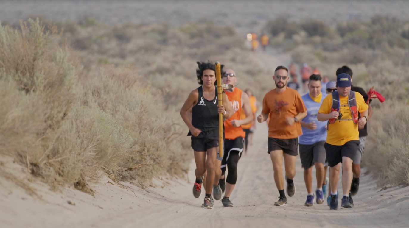 A group of Indigenous people run outside during a cultural event.