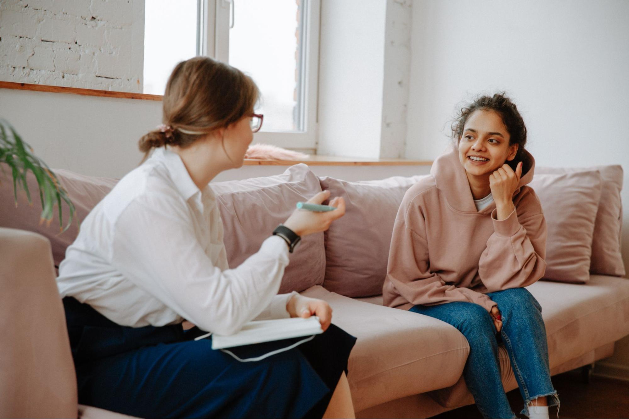 Two women talking on a couch with one writing notes