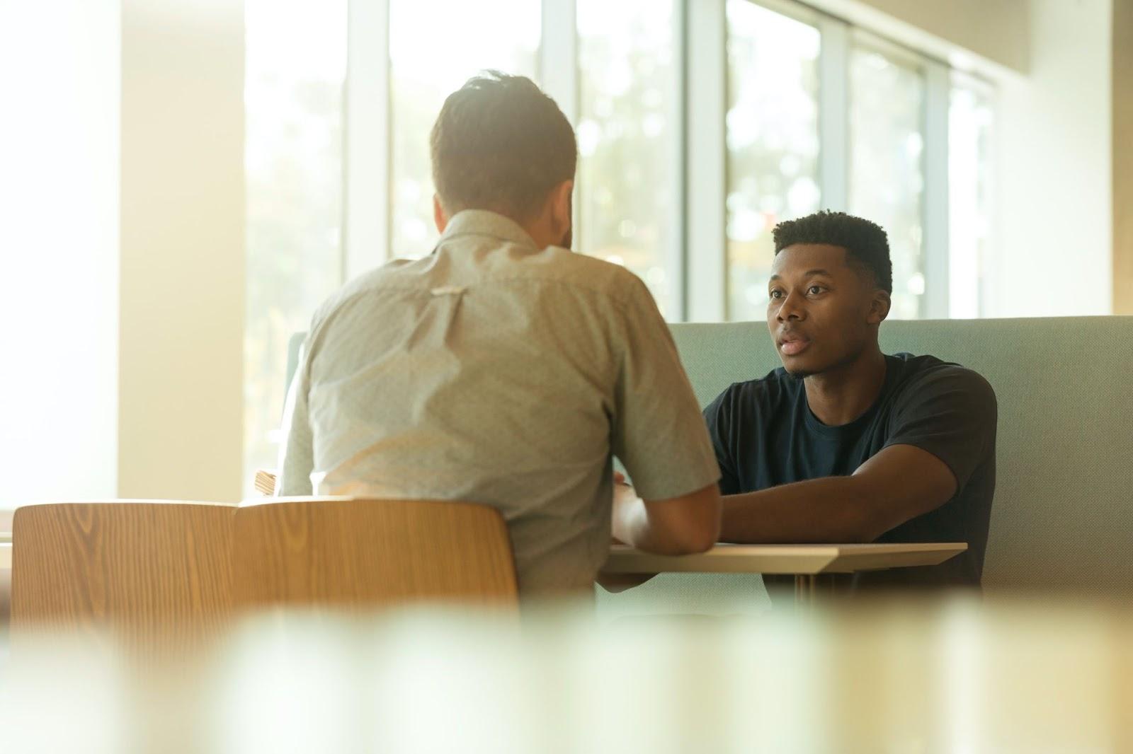 Two people sitting across from each other at a small table talking