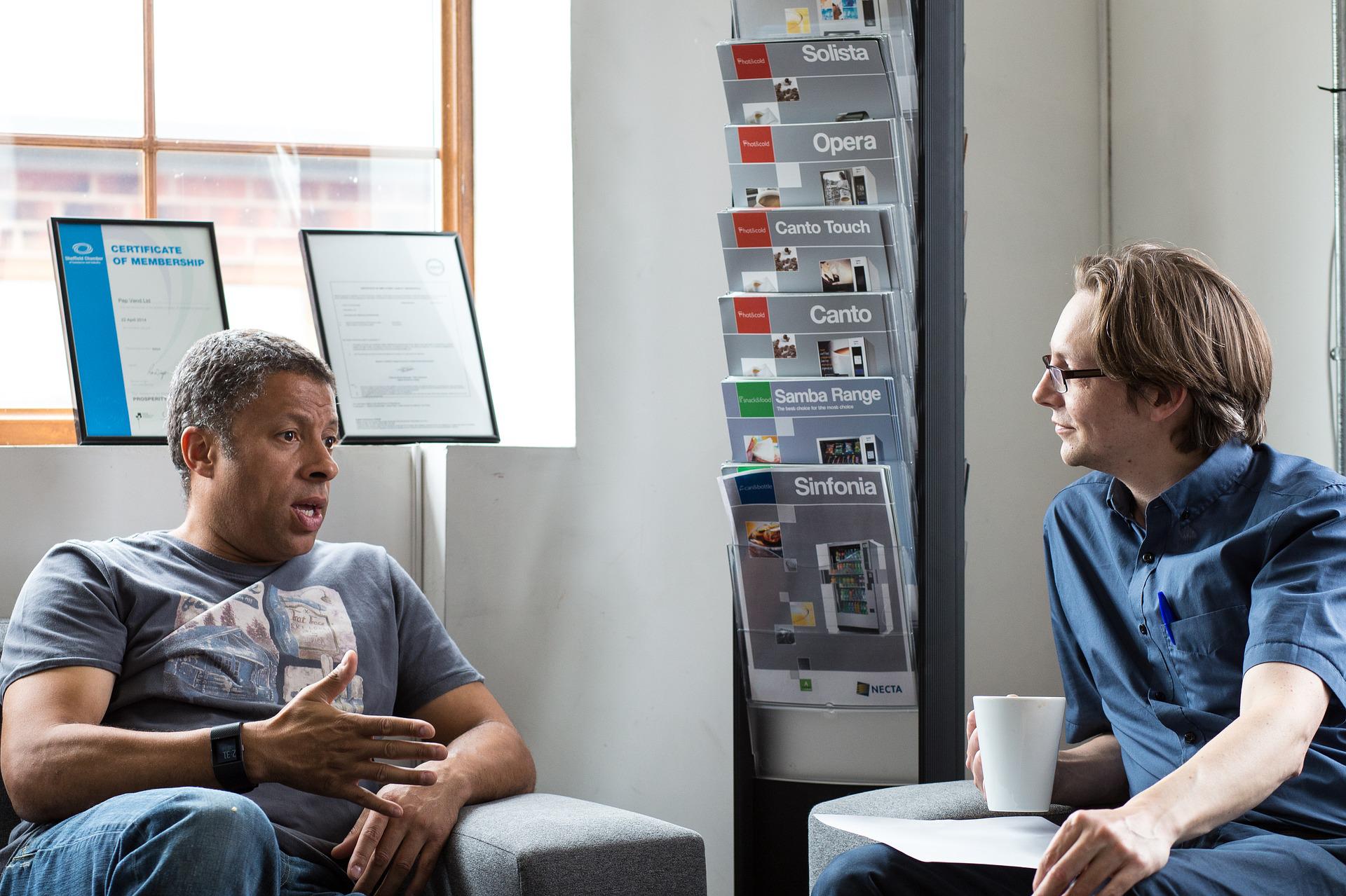 Two people sitting in padded armchairs and talking to each other.