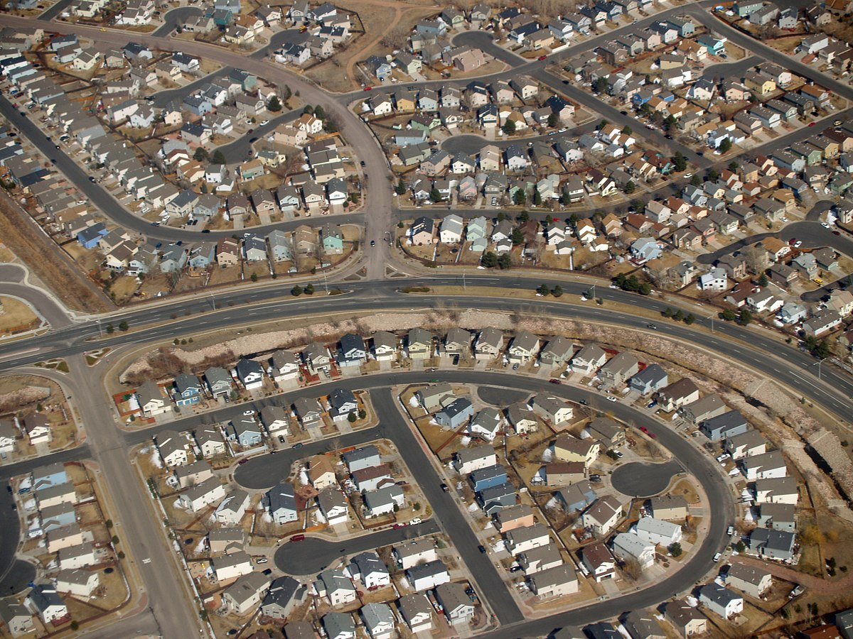 Aerial view of a subdivision with several cul de sacs with houses that have similar shapes and mostly fill their lots. Very little trees or green.