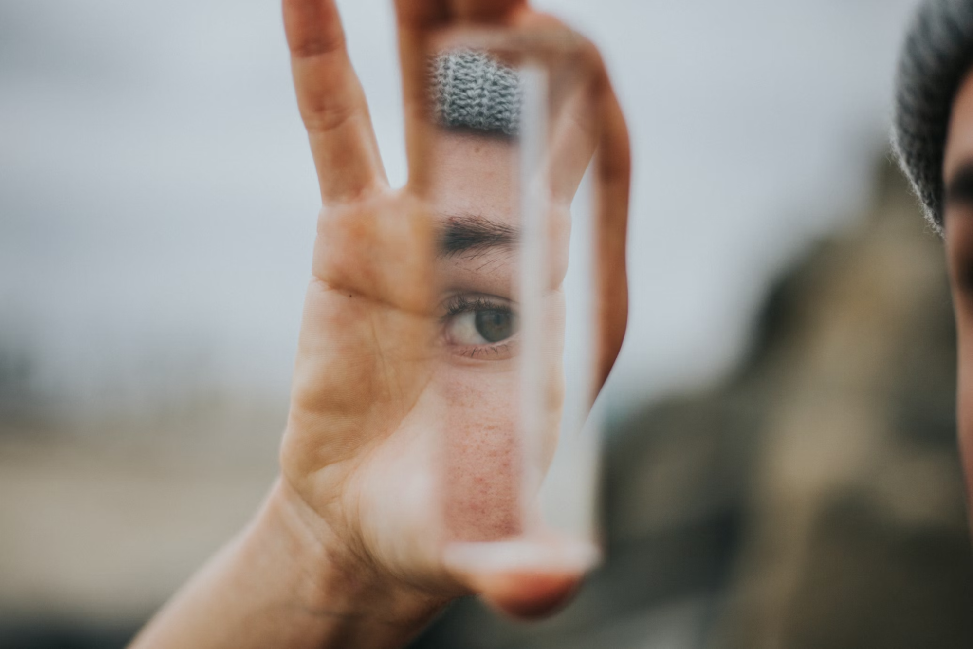 An image of a hand holding a small mirror that is reflecting one of the holder's eyes, eyebrows, and cheeks.