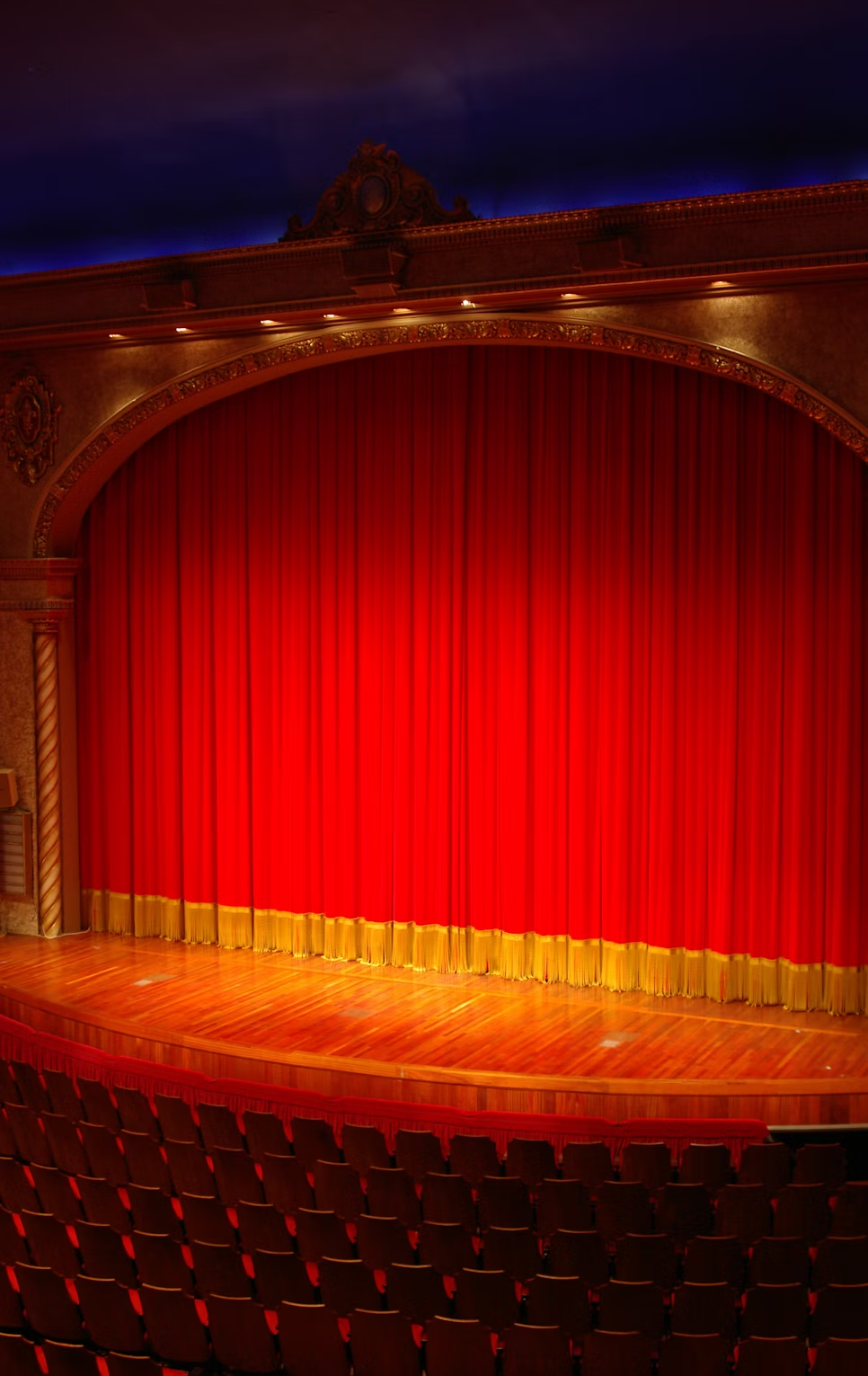 An empty theater stage with the red stage curtain closed.