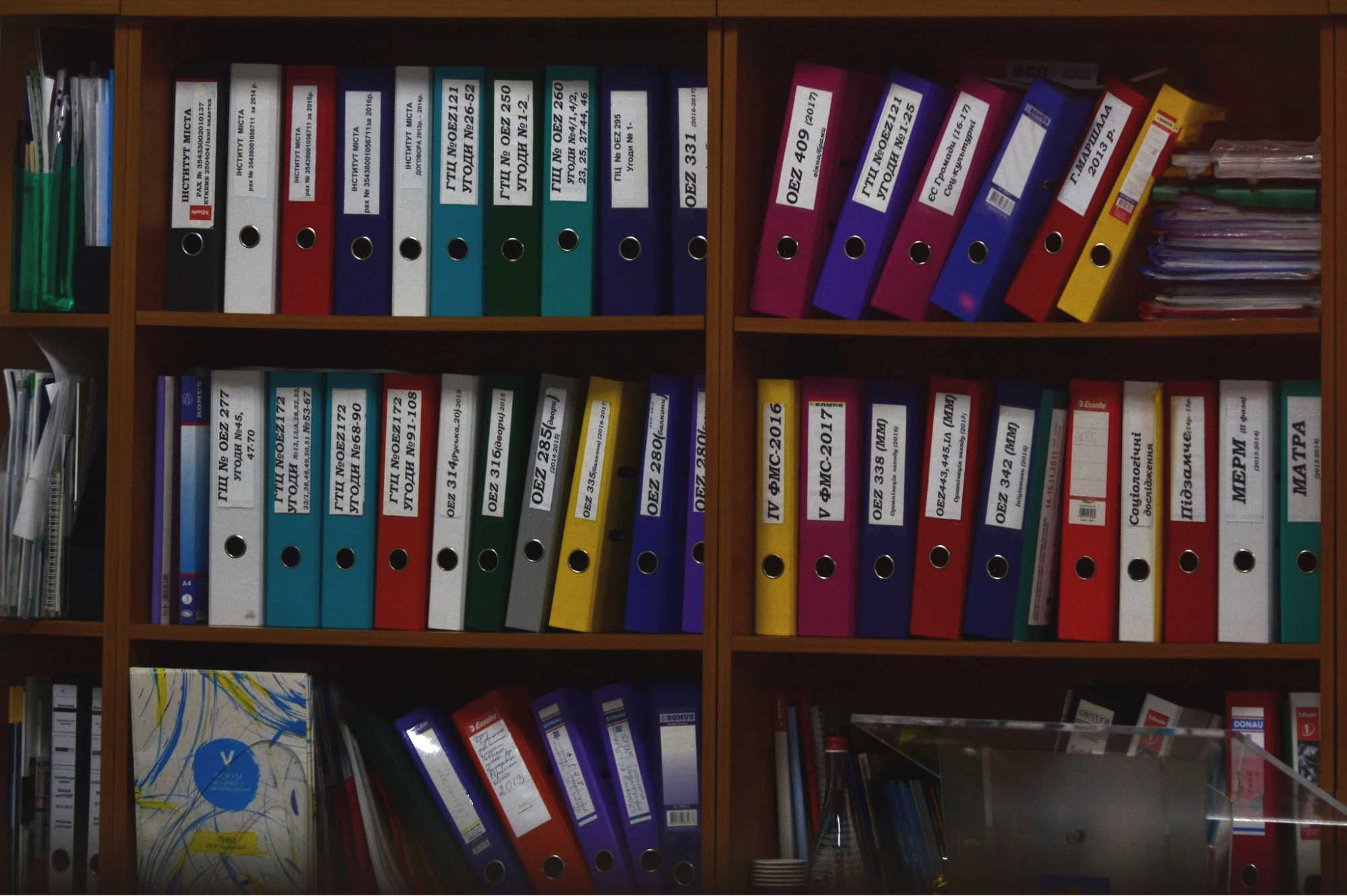 An image of multi colored binders on a set of brown shelves.