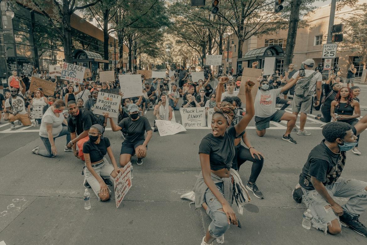 Protesters in the street on one knee. Some have signs that read "Black Lives Matter."