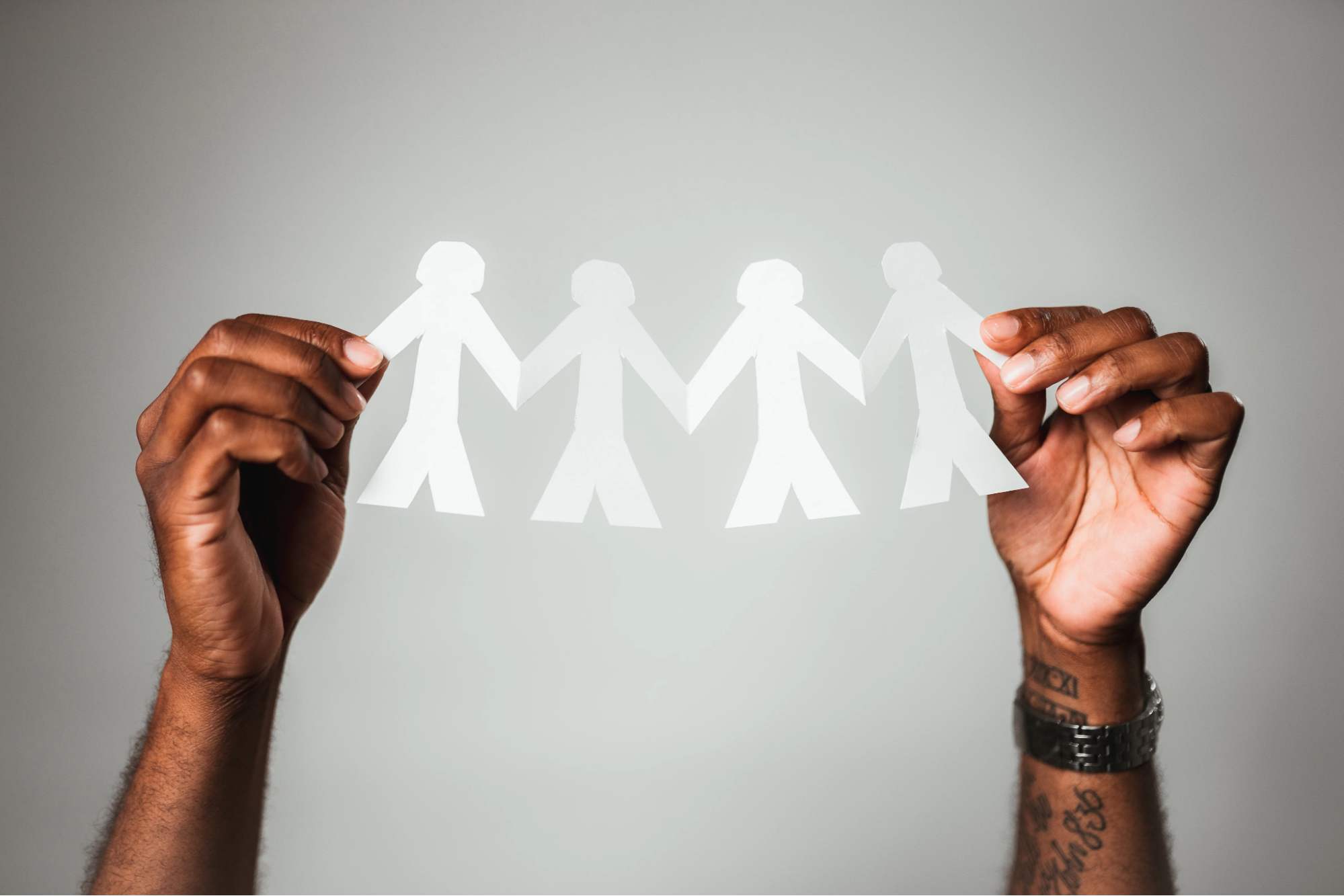 An image of two hands holding a white paper cutout of four stick figure people holding hands.