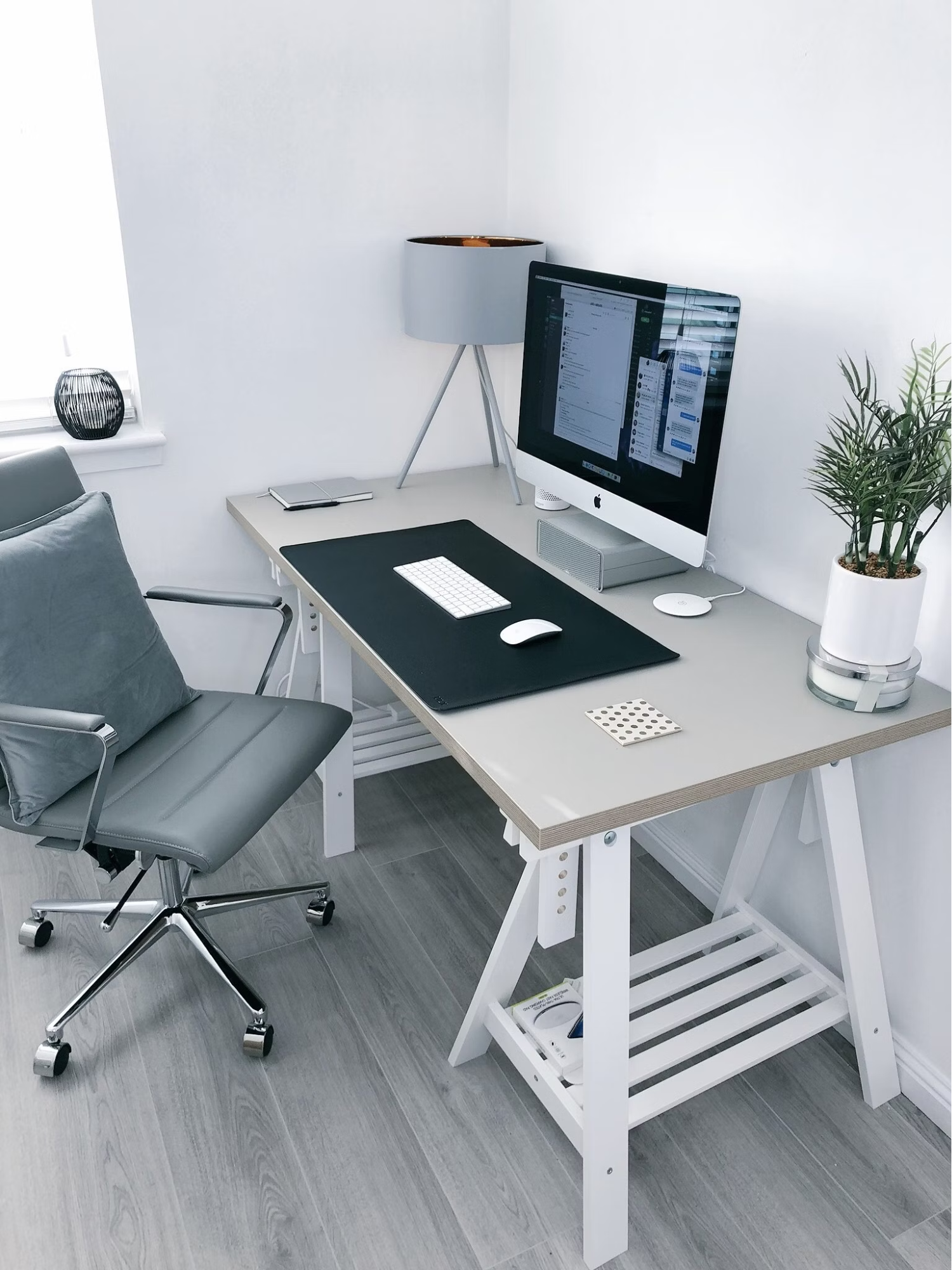 A grey leather office rolling armchair beside a white wooden computer desk with a computer screen.