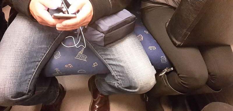 Example of manspreading on public transport. The man sits with his legs far apart, encroaching on the space of the woman next to him, who keeps her legs pressed together.