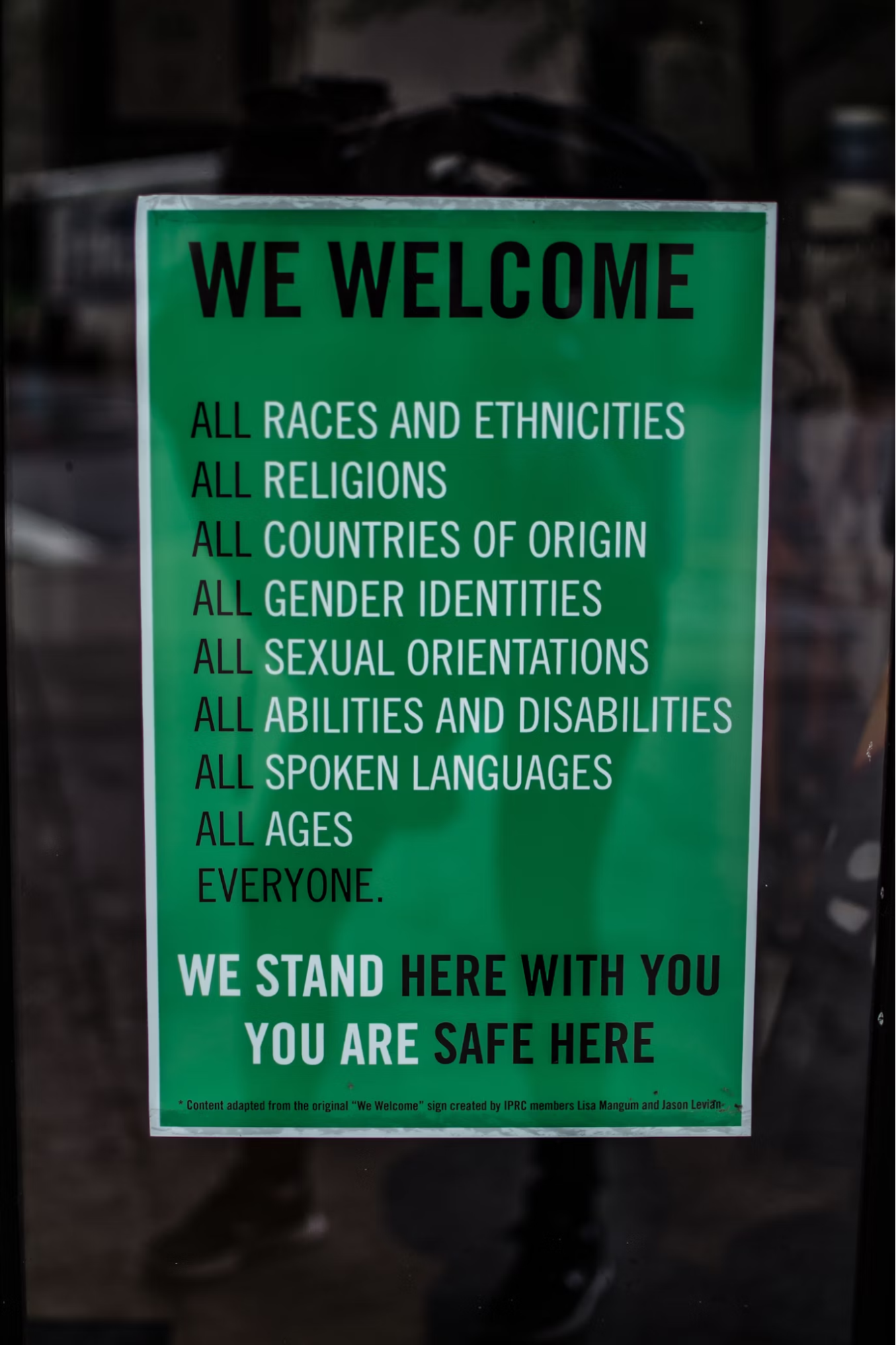 Green sign says "We welcome, all races and ethnicities, all religions, all countries of origin, all gender identities, all sexual orientations, all abilities and disabilities, all spoken languages, all ages, everyone. We stand here with you and you are safe here."